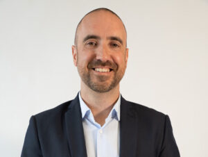 Anthony Gallace smiling in a navy blazer against a plain white background.
